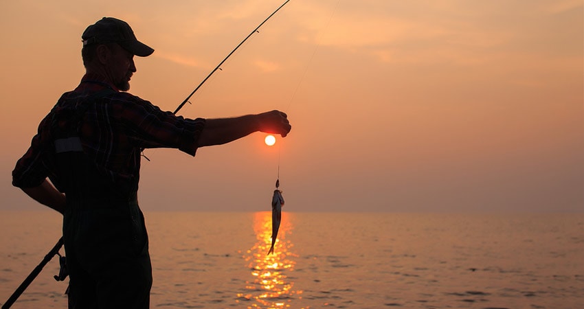 Man holding fish with sunset in background