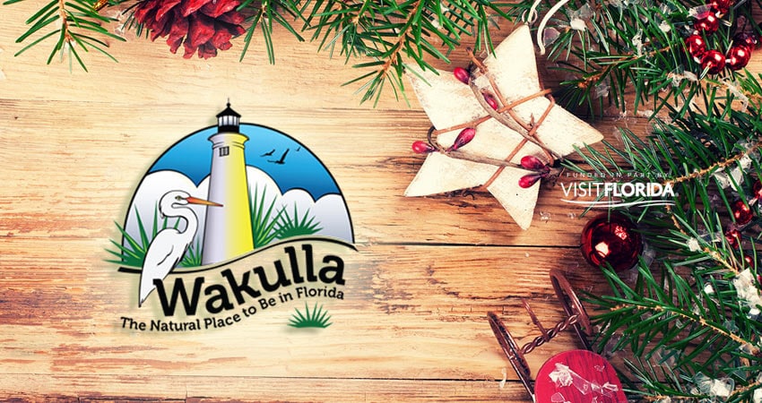 visit wakulla logo with wodden background with evergreen branches and festive Christmas ornaments