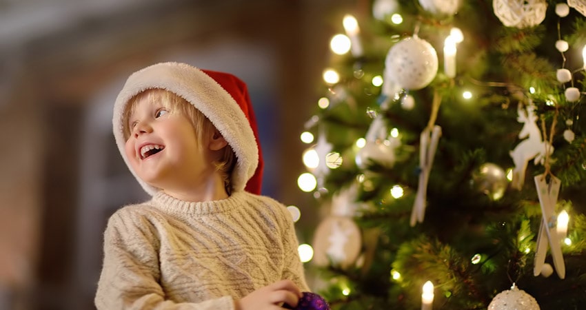 Little boy with Santa hat smiling next to Christmas tree