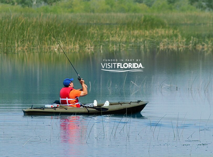 Man fishing off kayak with visit florida logo