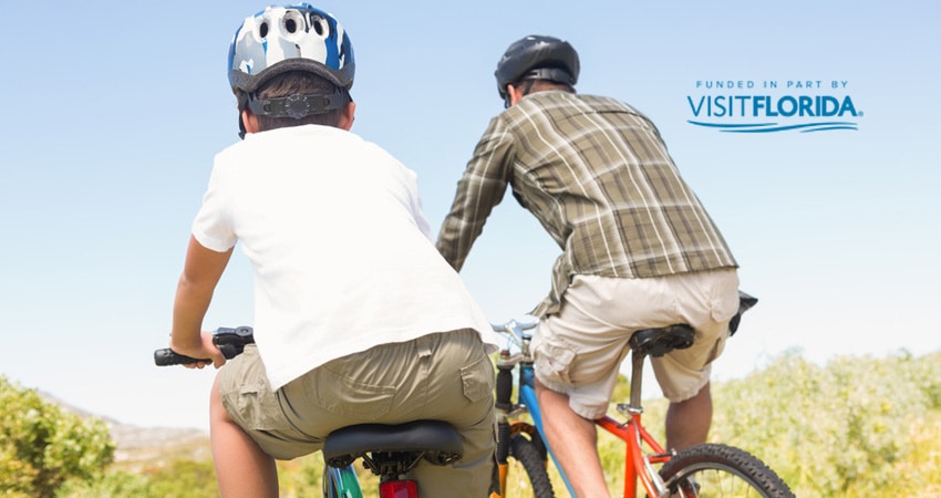 Father and son riding bikes with visit florida logo