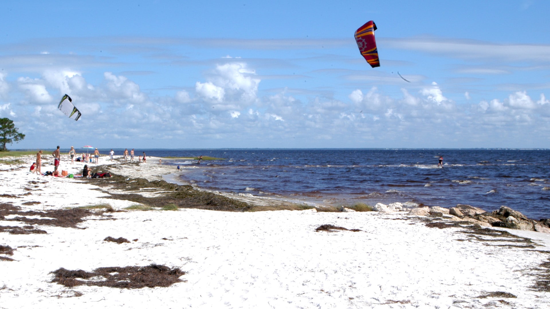 People on beach looking at water and kite surfing