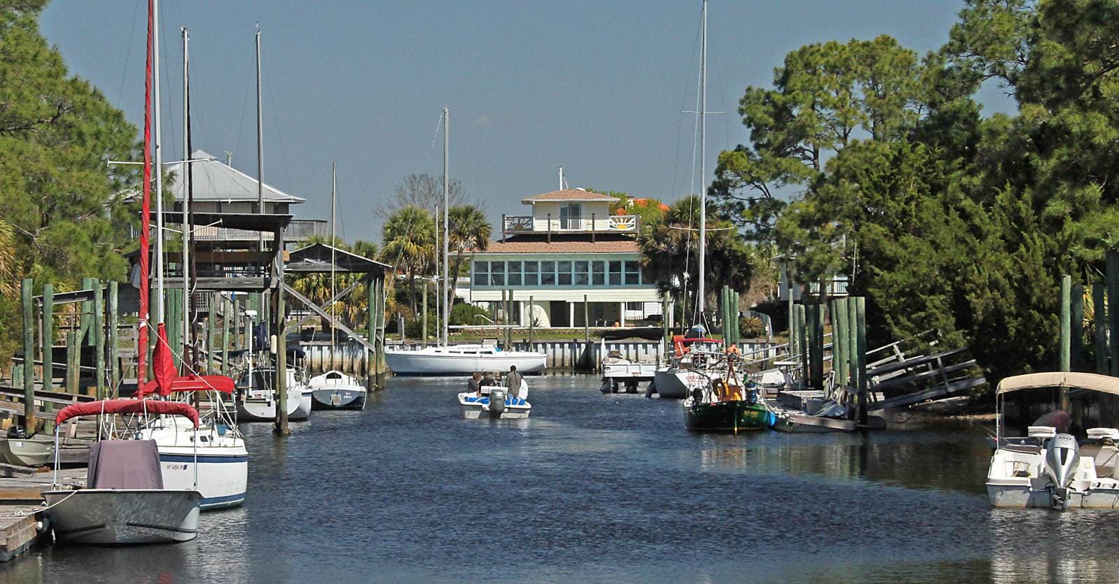 Image of water leading up to a building with boats on either side and one boat driving up the middle in Shell point