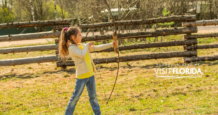 Girl pulling back wooden bow with visit florida logo