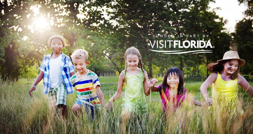 5 children holding hands running through field with visit florida logo